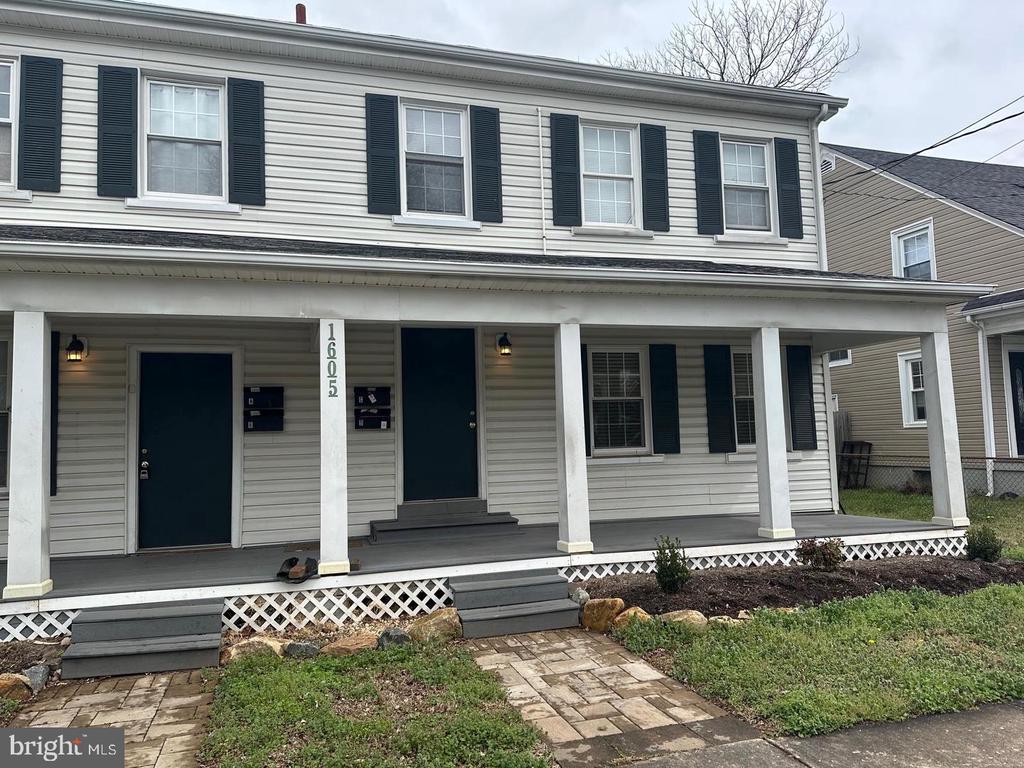 Two-story home with dark shutters, two front doors, and a long covered porch.