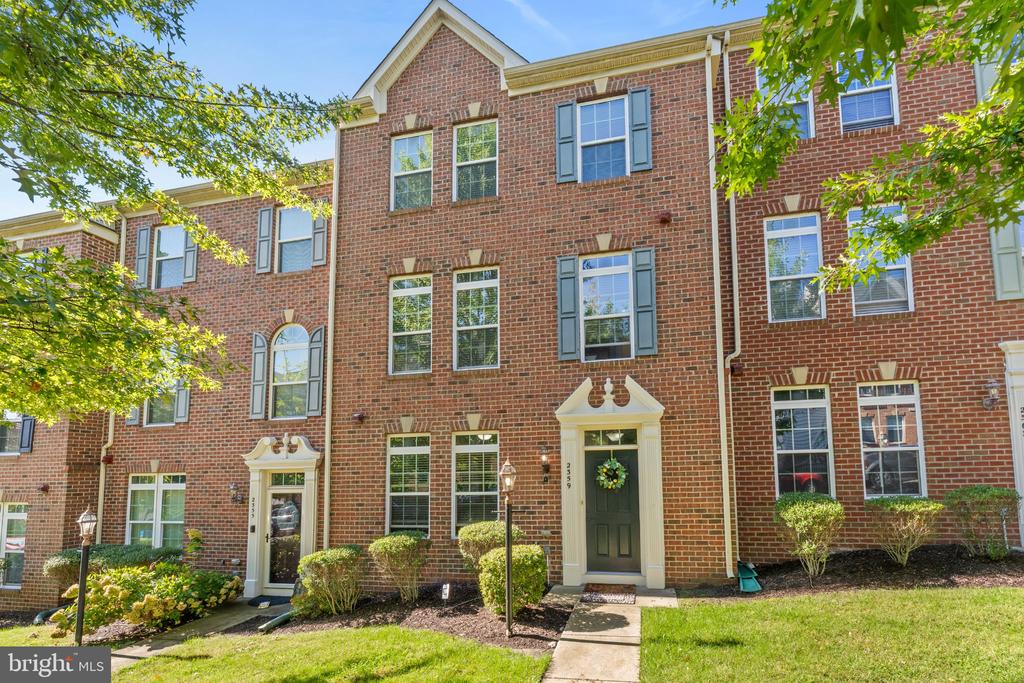 Red-brick townhouse with gray shutters, a green front door, and a landscaped entry.