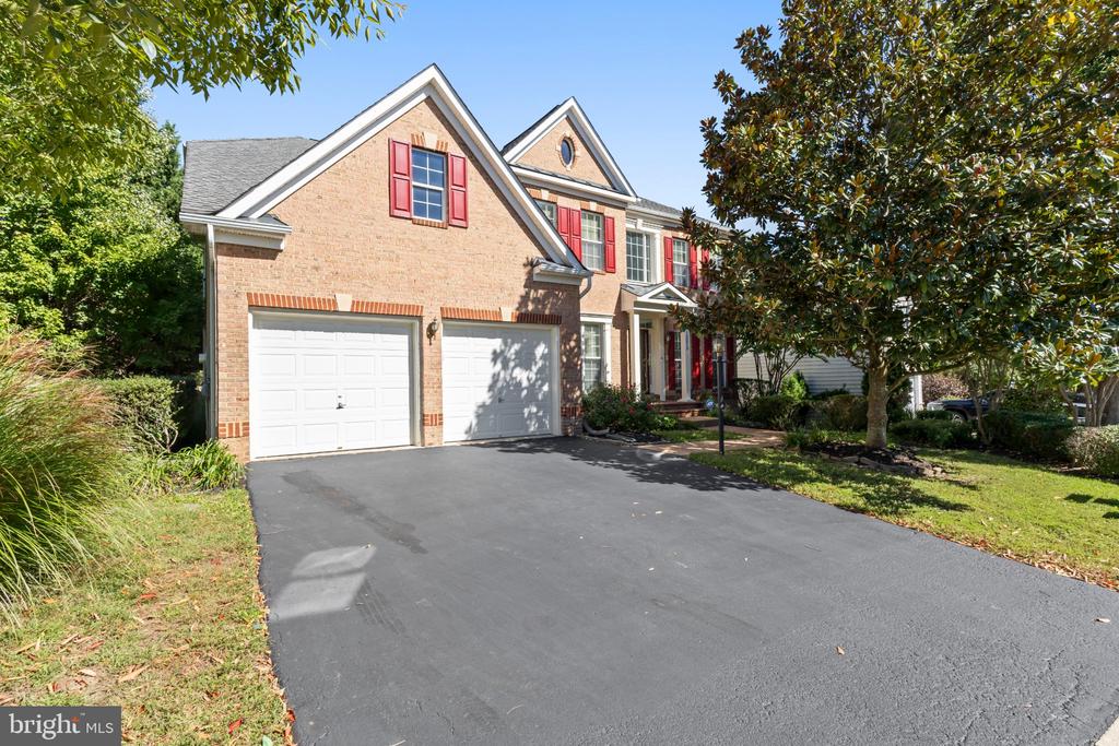 Brick building with red shutters, two garage doors, and a wide driveway.