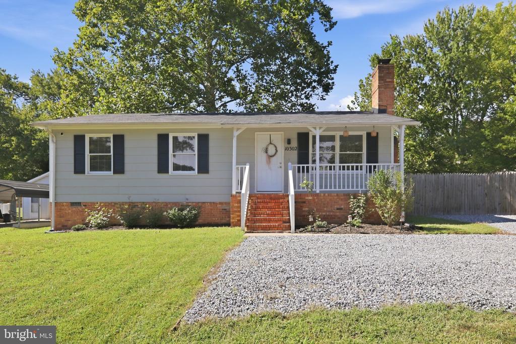 Single-story gray house with dark shutters, brick steps, and a gravel driveway.