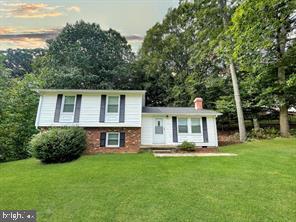Split-level home with white siding, brick lower facade, covered entry, and a broad lawn.