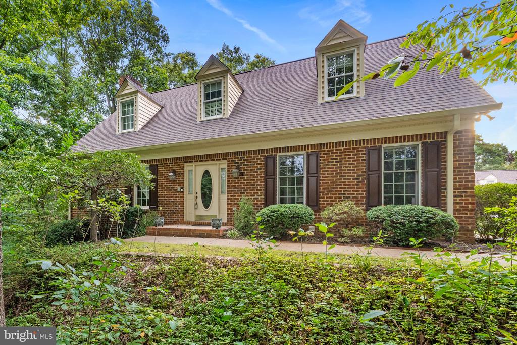 Brick house with three roof dormers, dark shutters, and an oval-glass front door.