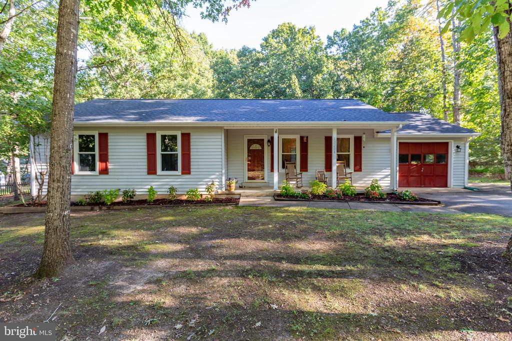 Single-story white house with red shutters and garage door, surrounded by mature trees.