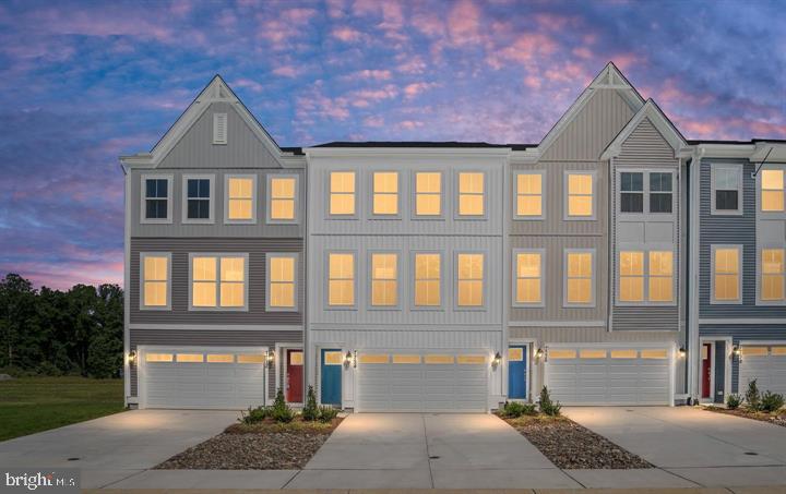 Attached gray townhouses with peaked rooflines and glowing windows at dusk.