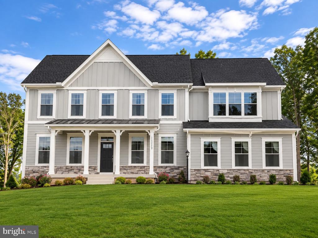 Two-story gray house with white trim, stone accents, a covered porch, and a broad green lawn.