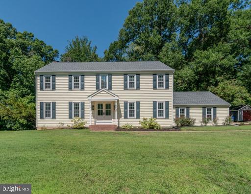 Two-story Colonial-style house with dark shutters, a central portico, and a broad green lawn.