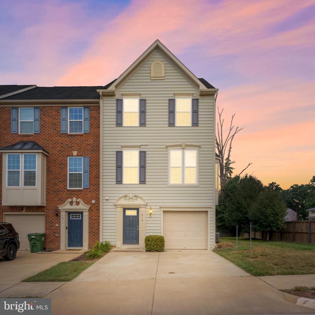 Three-story beige townhouse with blue shutters and attached garage at dusk.