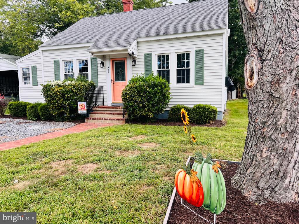 White house with green shutters and coral front door, seen behind a tree and pumpkin decorations.