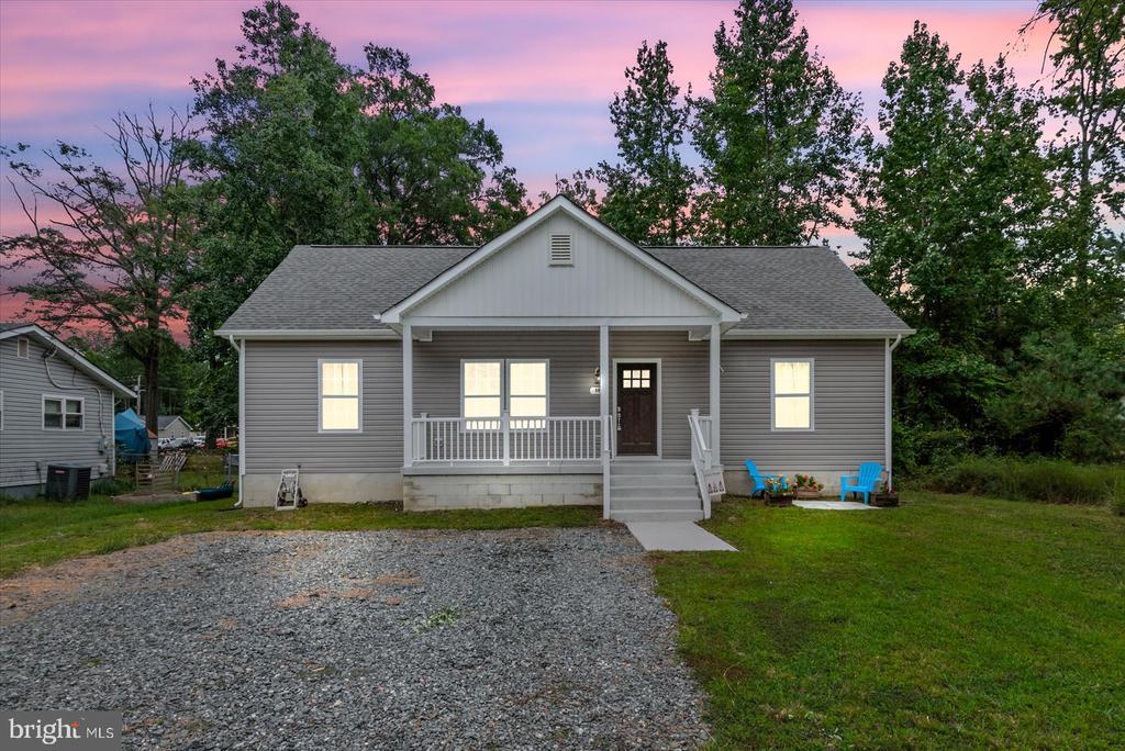Gray single-story home with a covered porch and gravel driveway beneath a pink dusk sky.