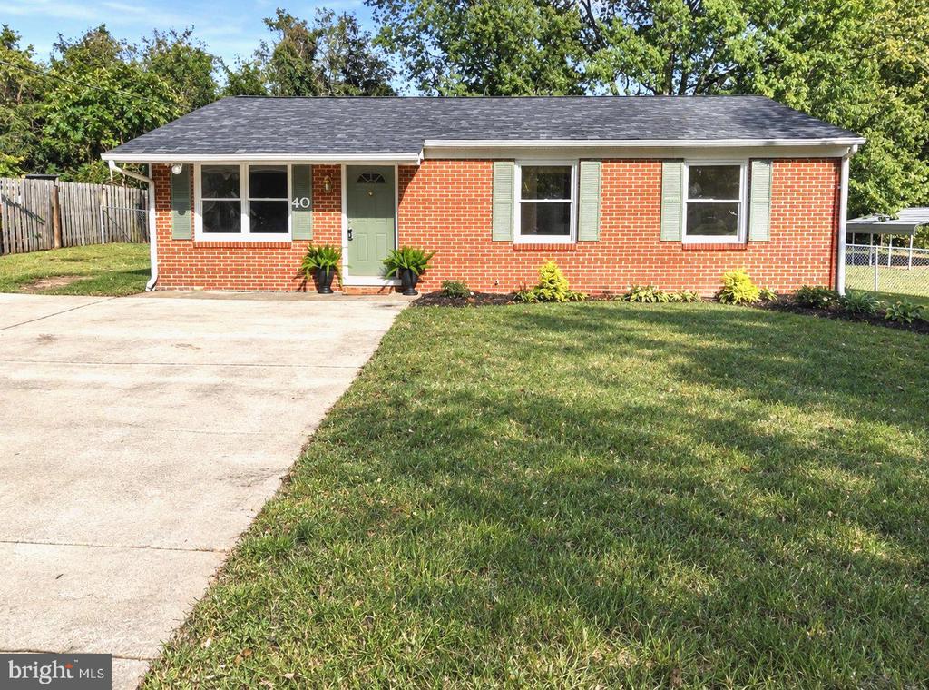 Single-story red brick house with pale green shutters, a concrete driveway, and a front lawn.
