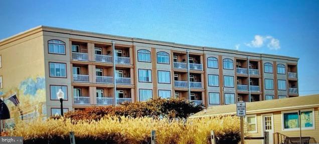 Multi-story tan building with balconies, arched windows, and landscaped grounds.