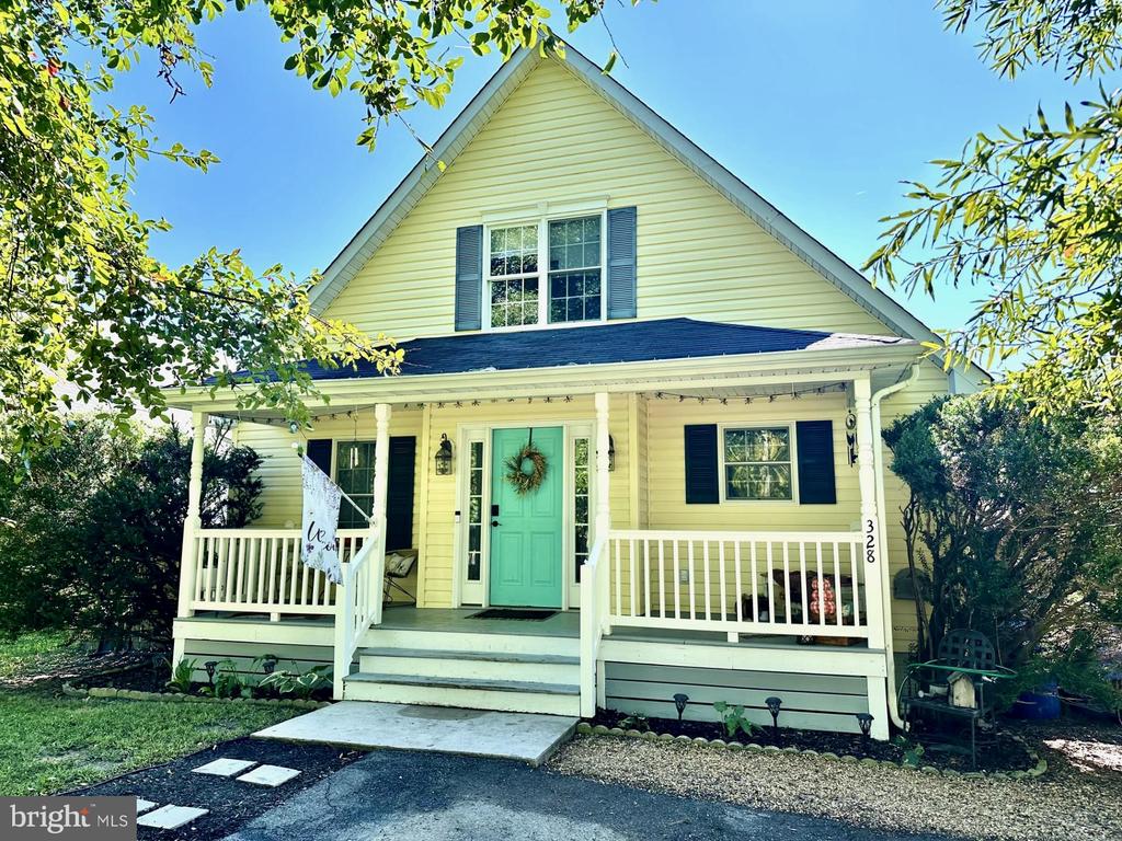 Pale yellow two-story house with a covered porch, turquoise door, and blue shutters.