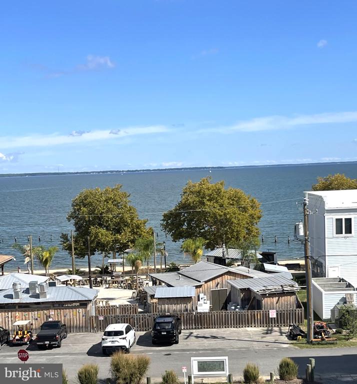 Waterfront view across low buildings and trees toward the water and distant shoreline.