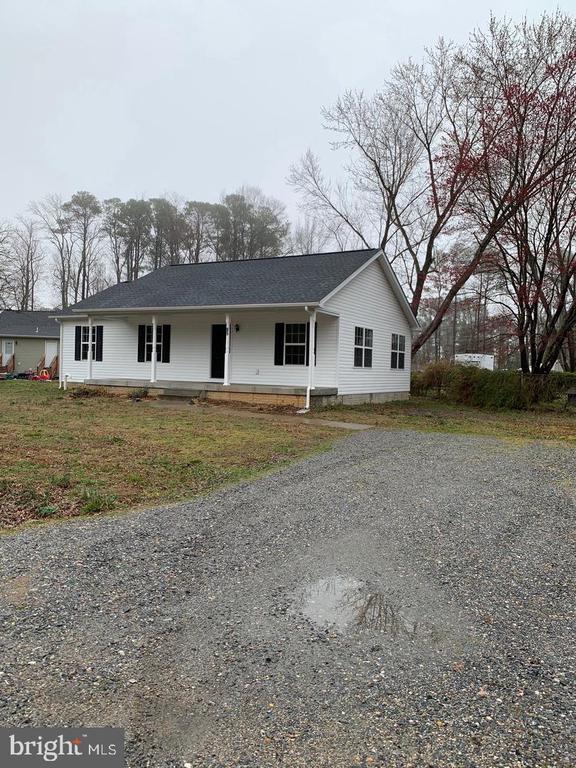 White single-story house with black shutters beside a broad gravel driveway.