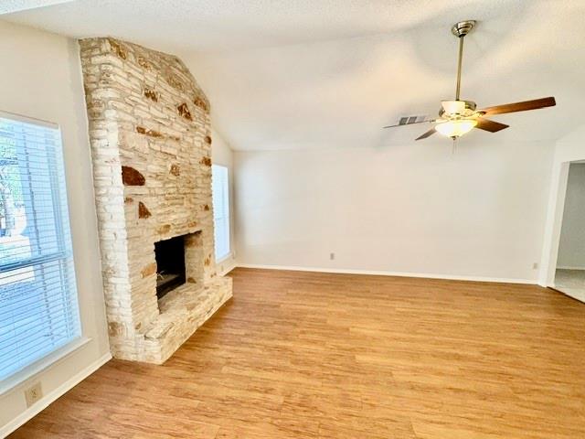 Empty living room with a tall stone fireplace and warm wood flooring.