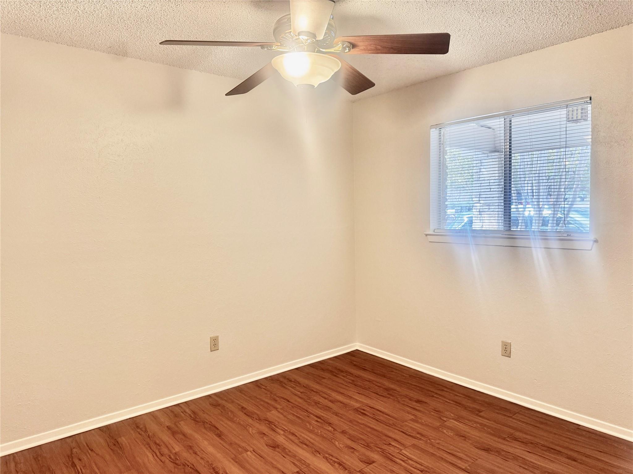 Empty room with wood flooring, a ceiling fan, and a window with blinds.