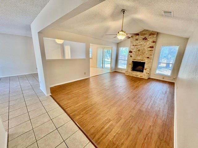 Vacant living room with hardwood floors and a stone fireplace beneath a vaulted ceiling.