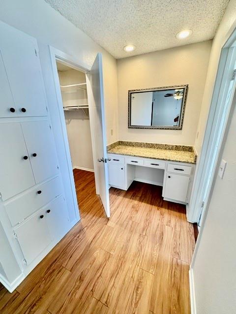Dressing room with built-in white cabinets, a granite vanity, framed mirror, and wood flooring.