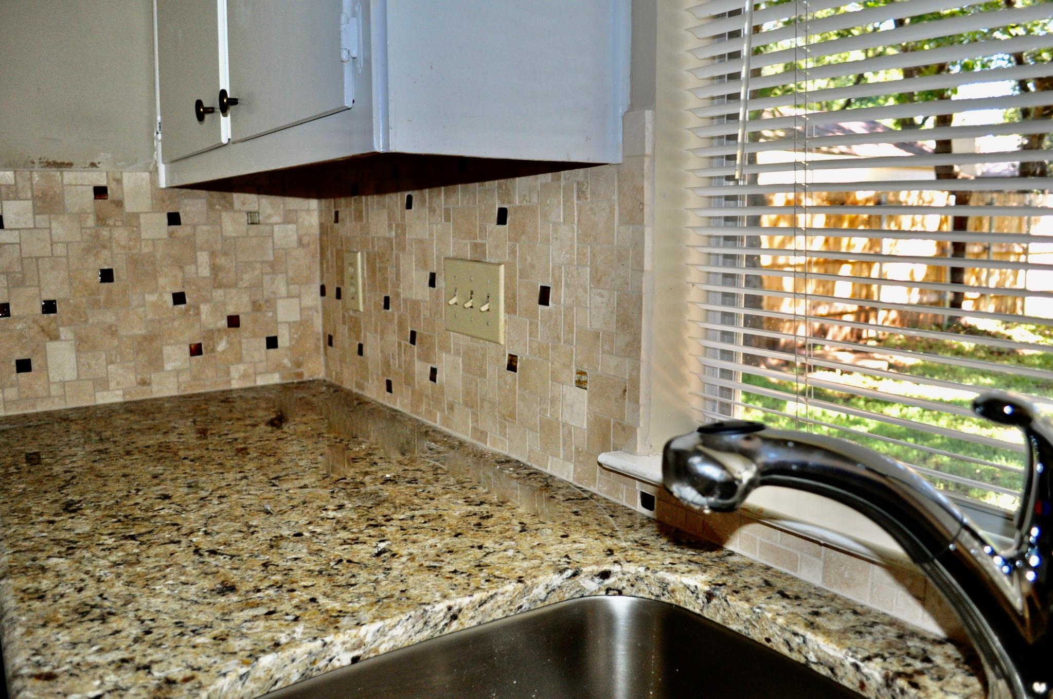 Kitchen corner with granite counters, tiled backsplash, and a stainless steel sink beneath a window.