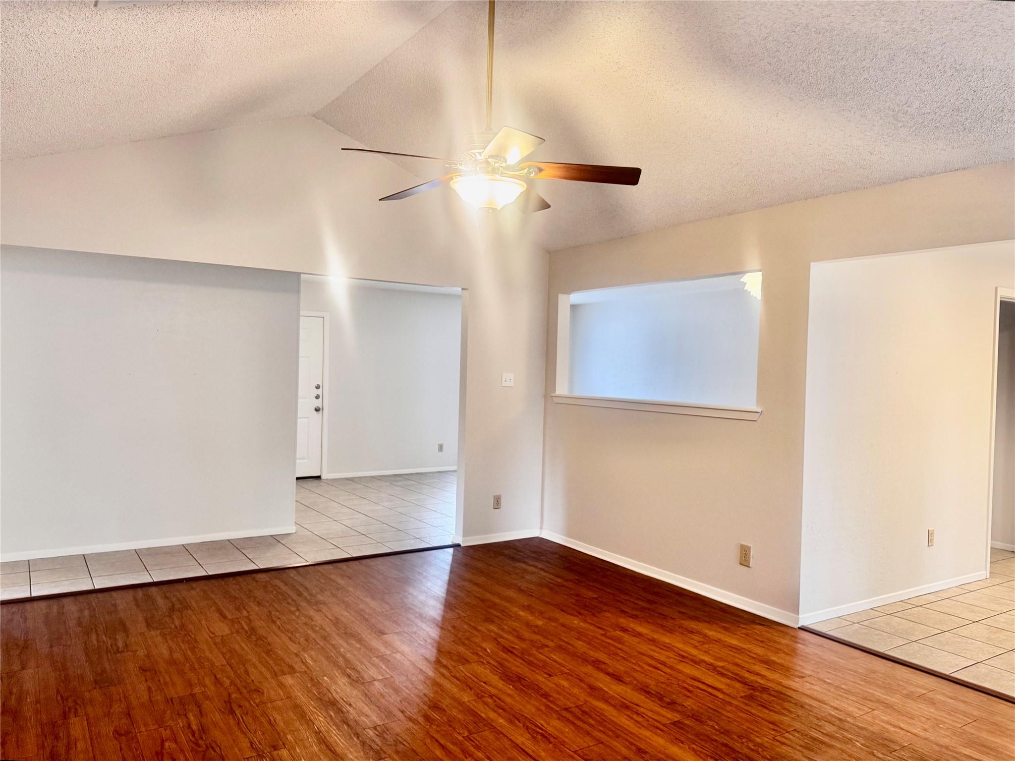 Vacant living room with wood flooring, ceiling fan, and wide pass-through opening.