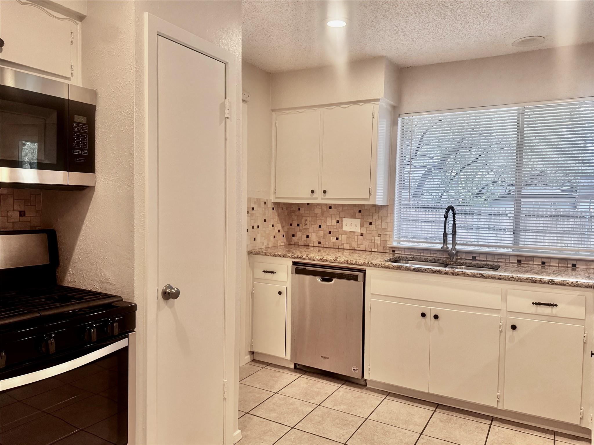 Kitchen with white cabinets, tiled backsplash, granite counters, and a sink beneath a wide window.