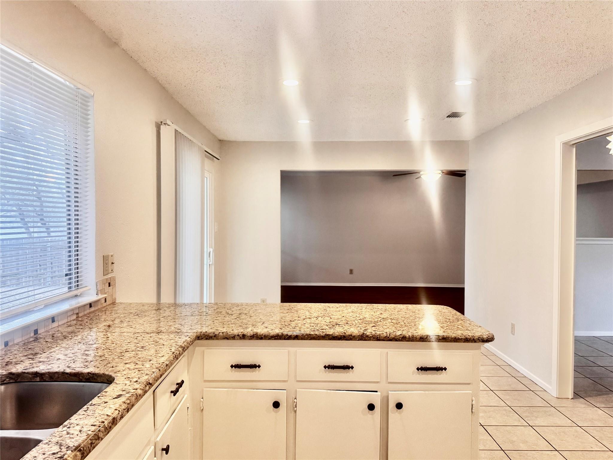 Vacant kitchen with granite peninsula, stainless-steel sink, white cabinets, and an opening to the living area.