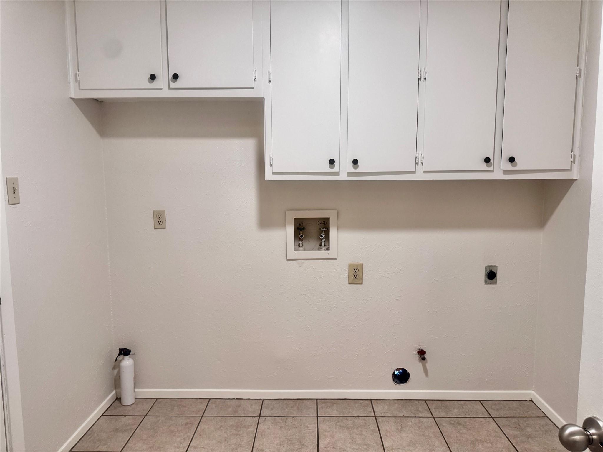 Empty laundry area with white cabinets, washer hookups, and a gray tile floor.