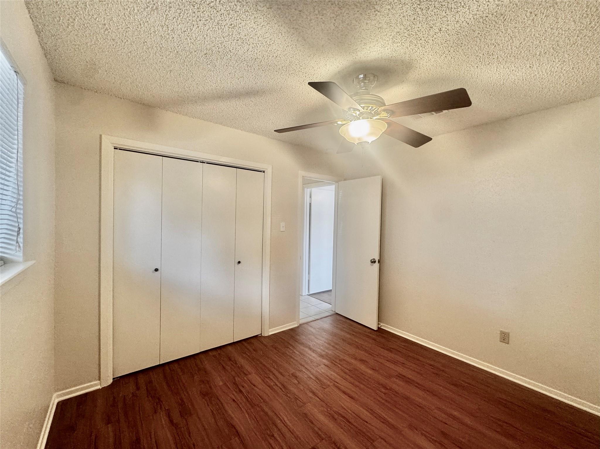 Empty bedroom with a large closet, ceiling fan, dark wood-look flooring, and an open door.