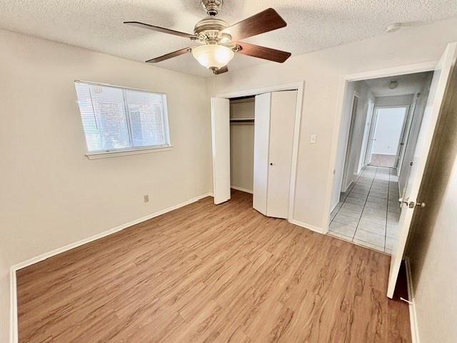 Empty bedroom with wood-look flooring, ceiling fan, window, and open closet.