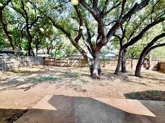 Backyard with mature shade trees, a wooden privacy fence, and a concrete patio.