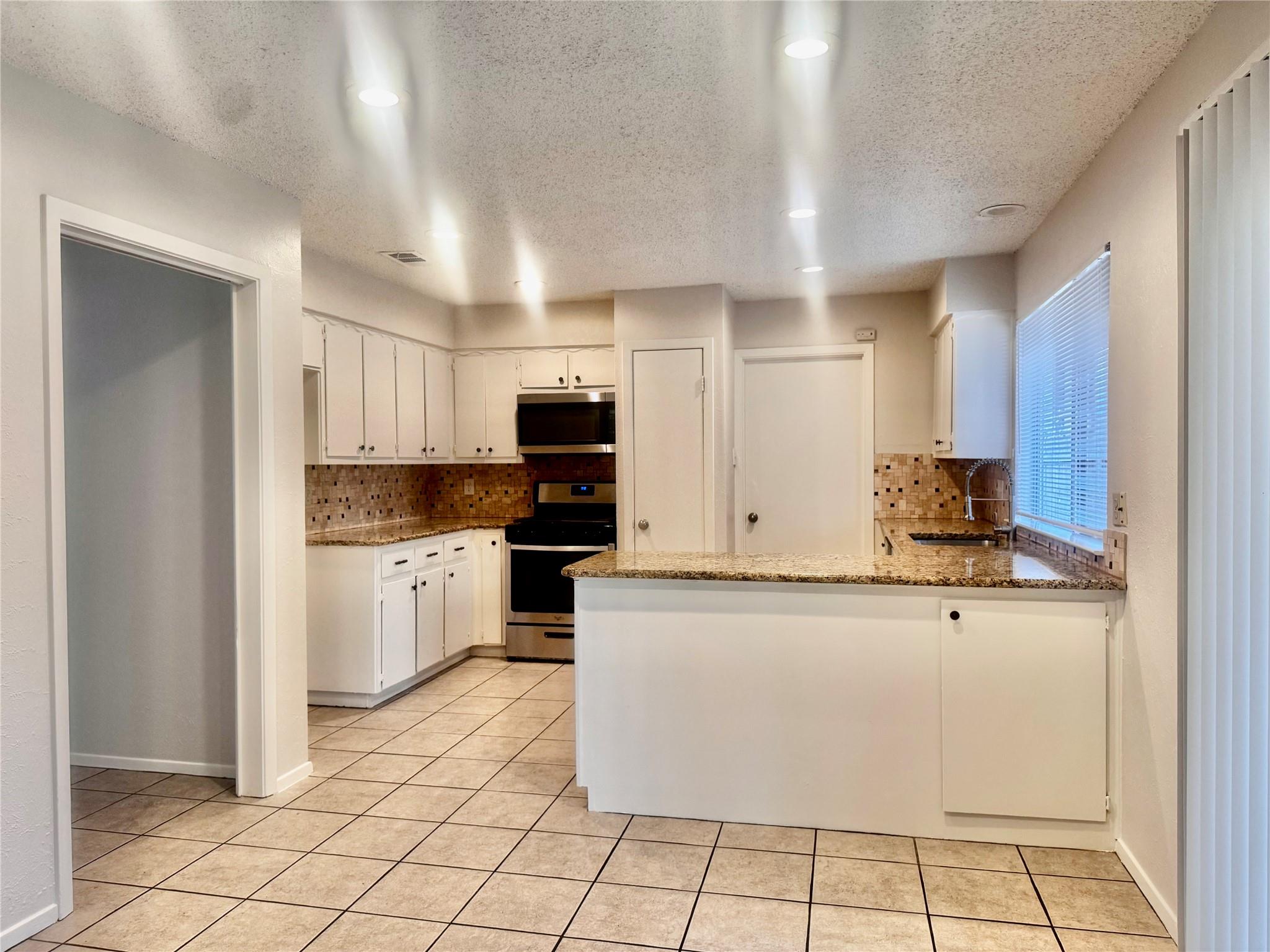 Kitchen with white cabinetry, black appliances, and a granite peninsula.