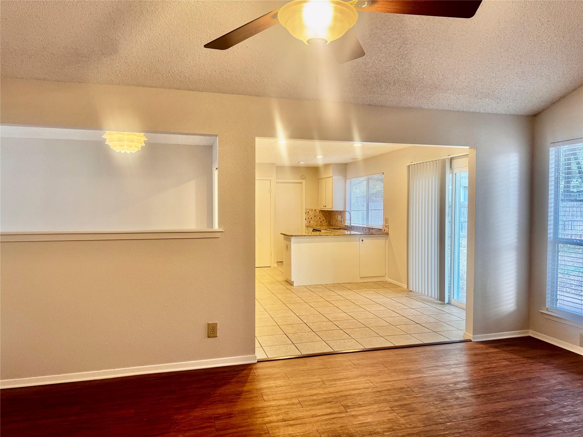 Vacant living area opening to a tiled kitchen with white cabinets and a peninsula.