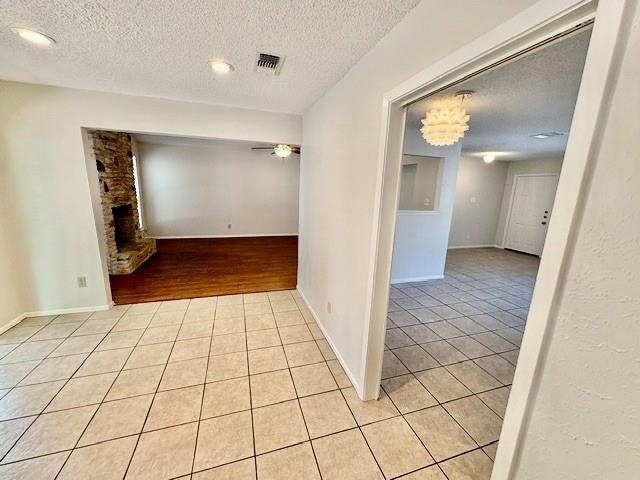 Unfurnished interior with tiled floors, an adjoining hardwood living area, and a stone fireplace.