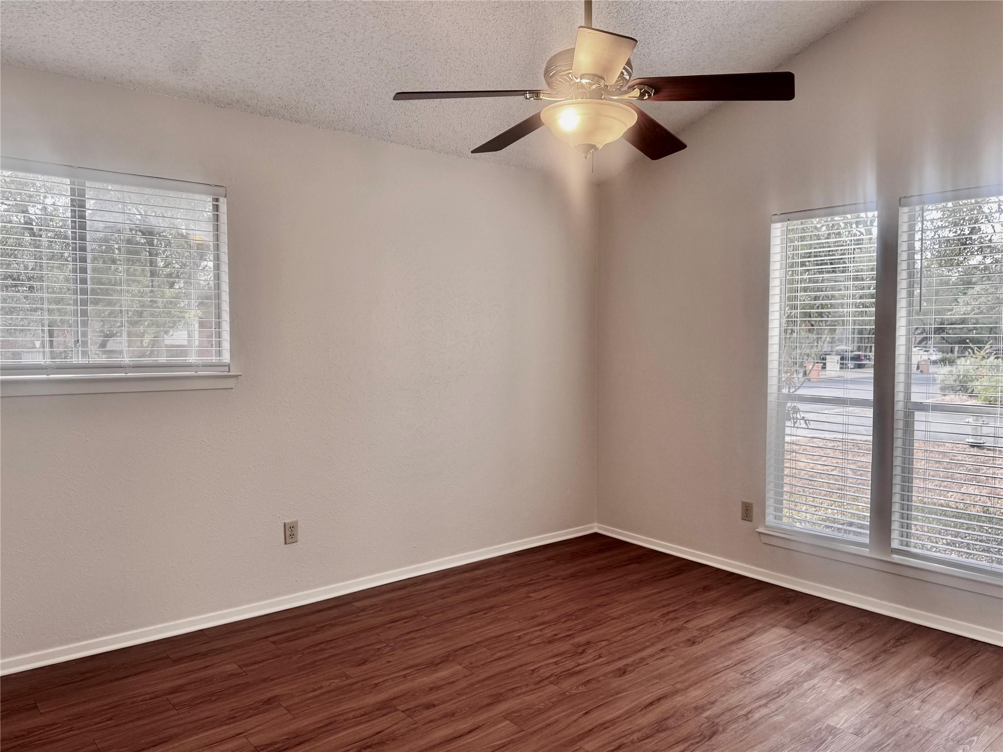 Empty room with wood-look flooring, a ceiling fan, and windows with blinds.