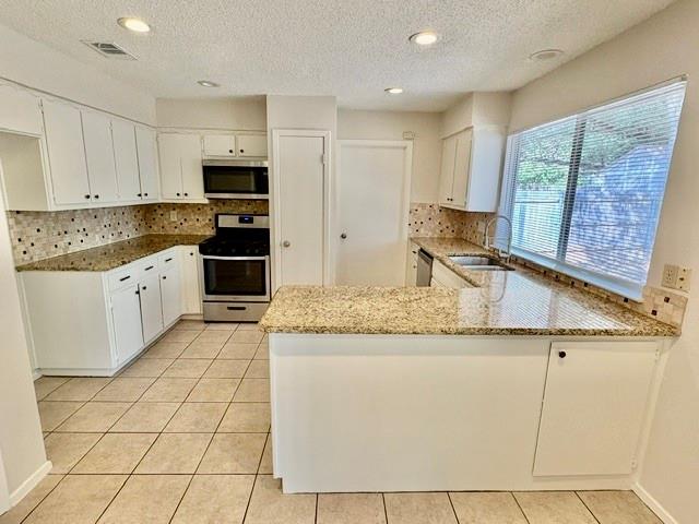 Vacant kitchen with white cabinets, granite counters, stainless steel appliances, and a large window over the sink.