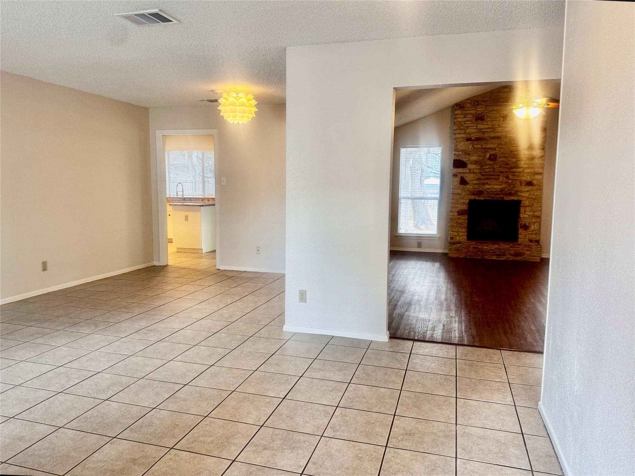 Tiled dining area opening to a living room with a stone fireplace and dark wood floors.