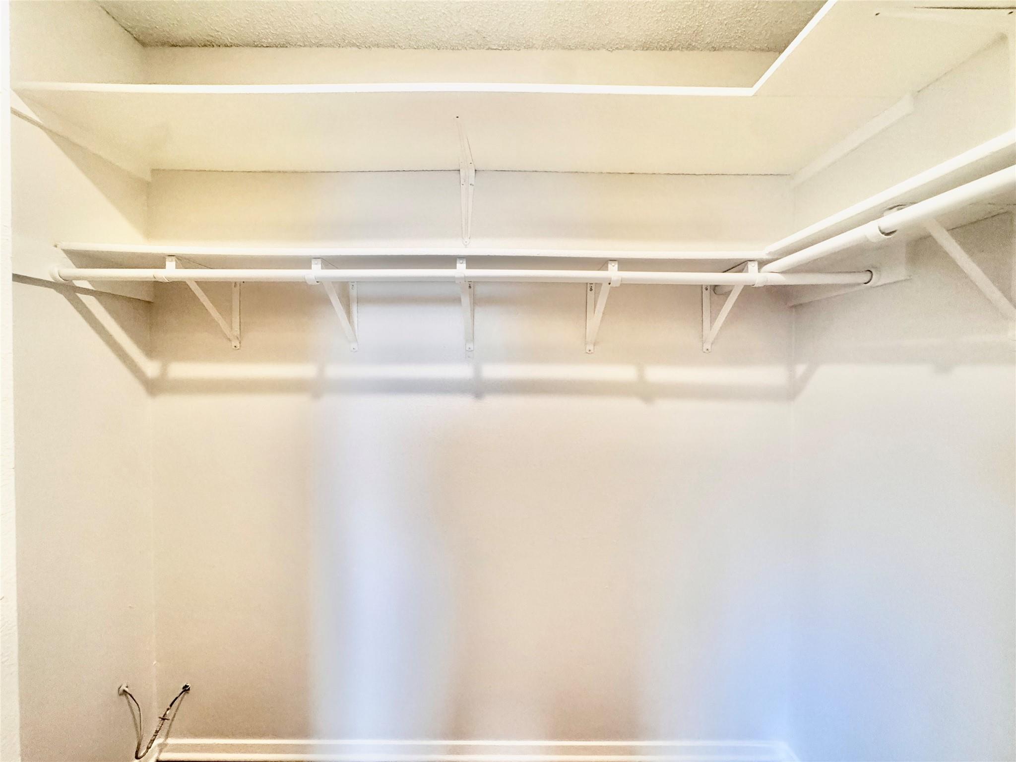 Empty walk-in closet with a high shelf and hanging rods along three walls.