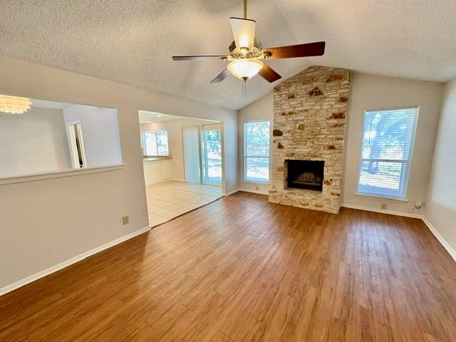 Unfurnished living room with wood-look floors, a tall stone fireplace, and a ceiling fan.