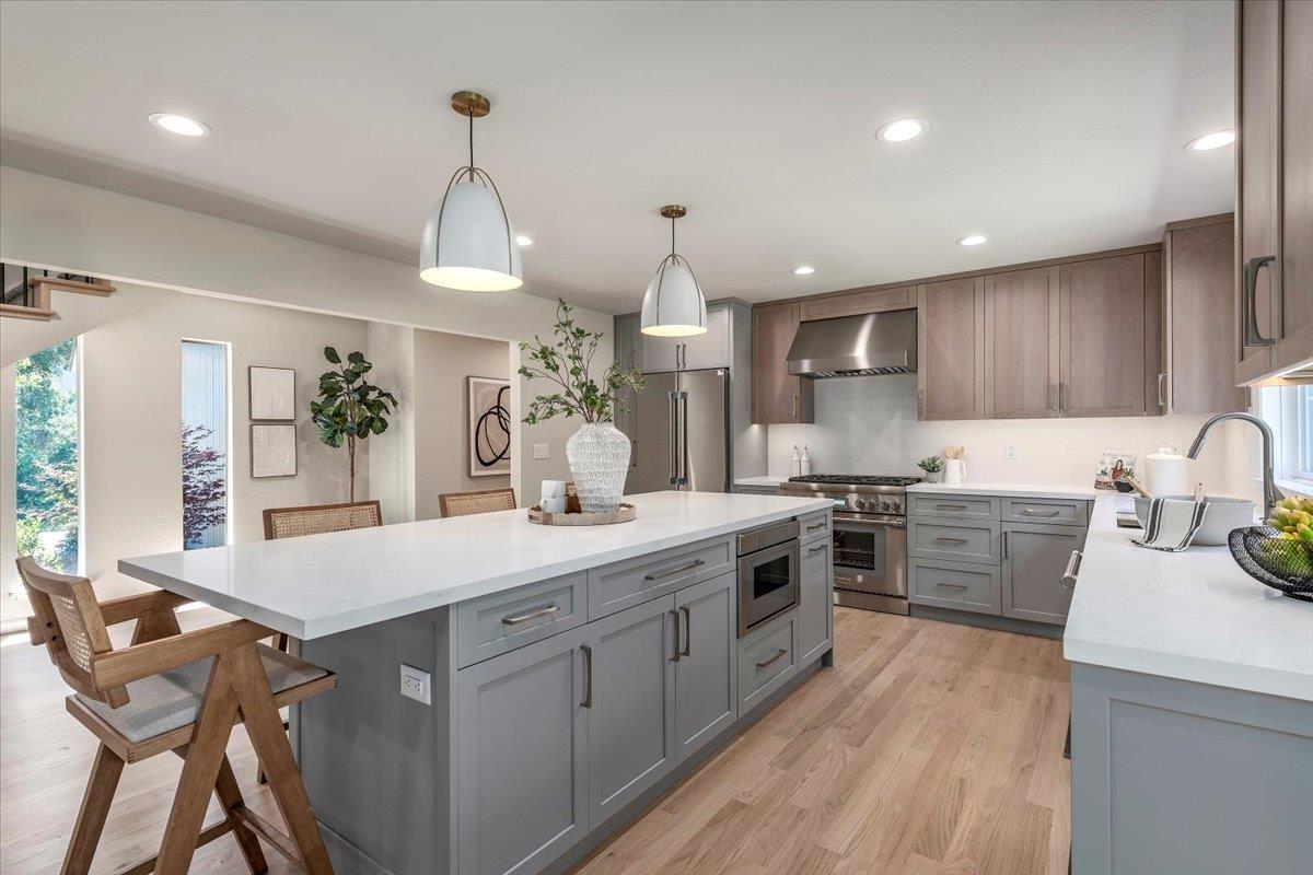 Staged kitchen with a large gray island, white countertops, warm wood cabinets, and stainless steel appliances.