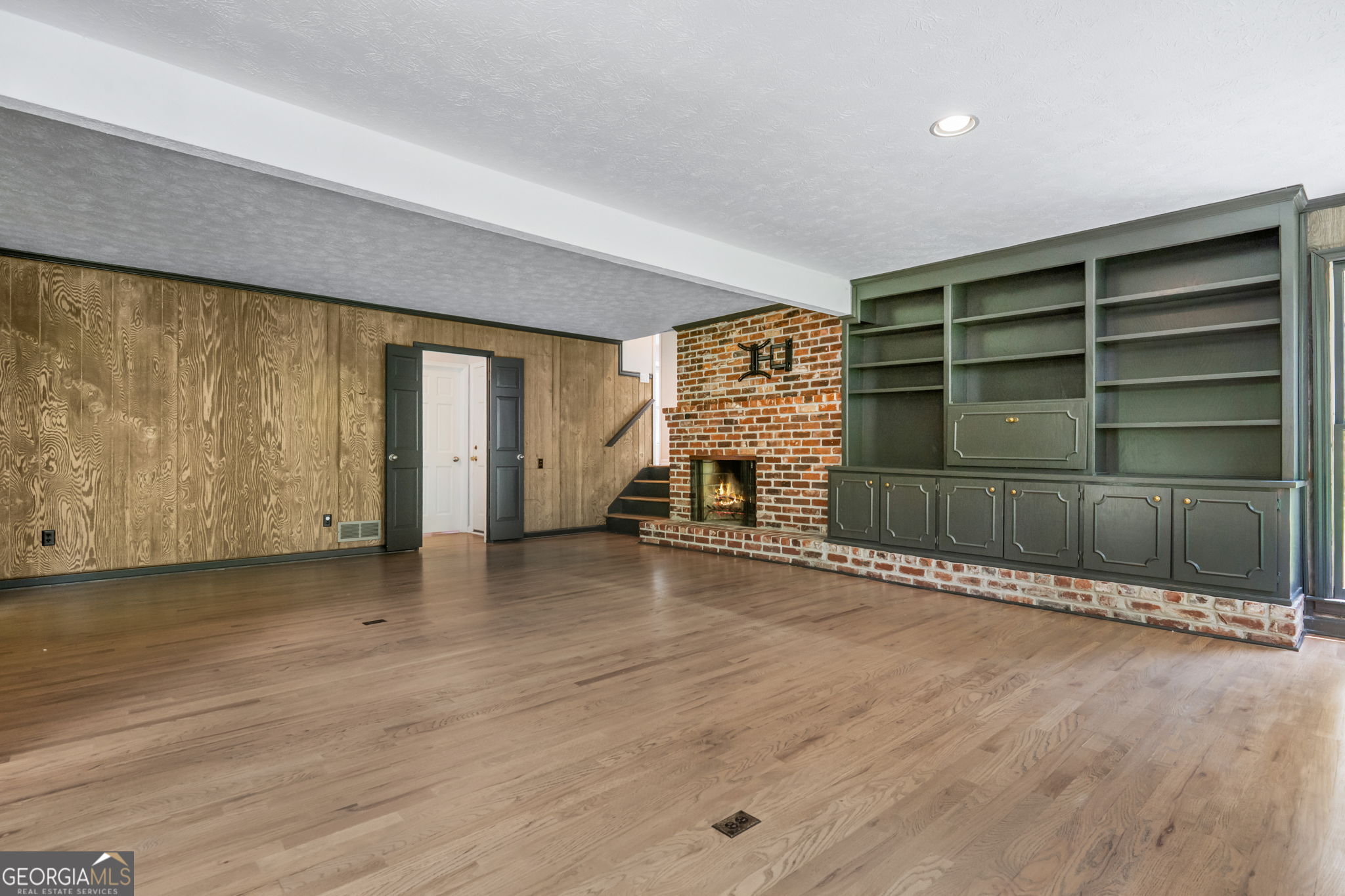 Empty living room with hardwood floors, a brick fireplace, and built-in shelving.