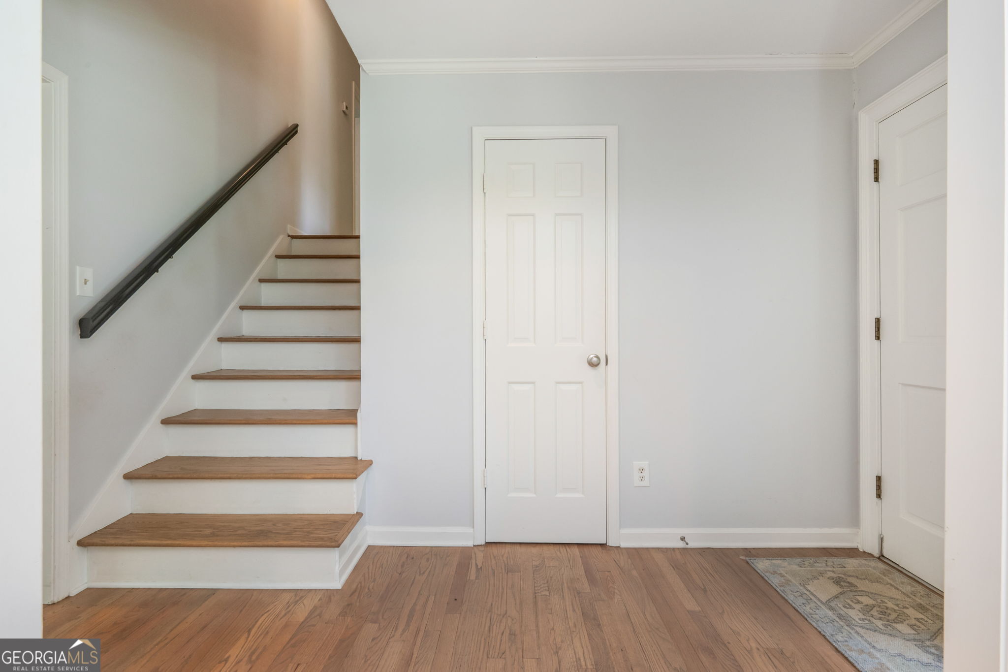 Entryway with hardwood floors, a staircase with wood treads, and two white paneled doors.