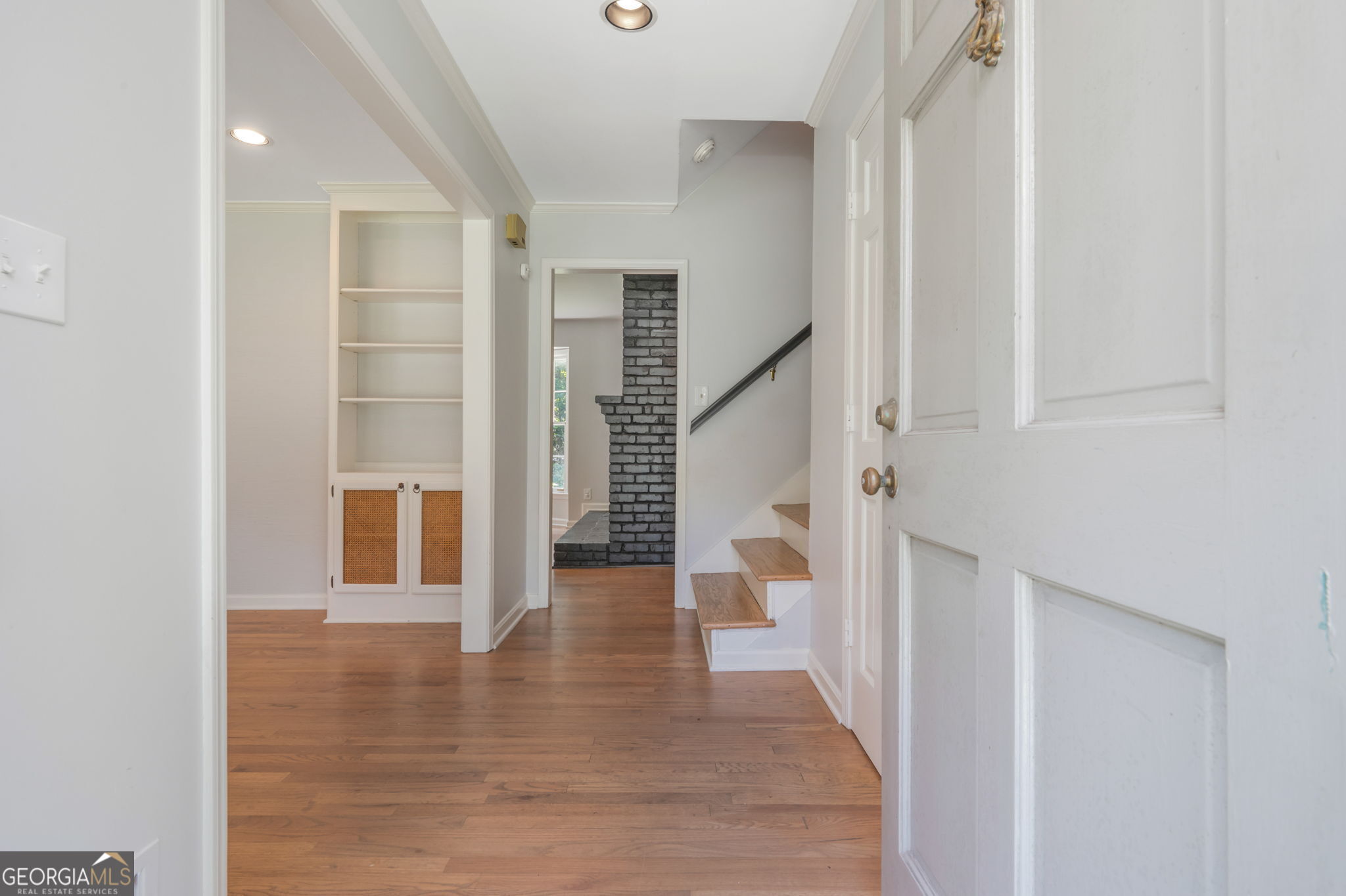 Entry hall with hardwood floors, built-in shelving, stairs, and a dark brick fireplace.
