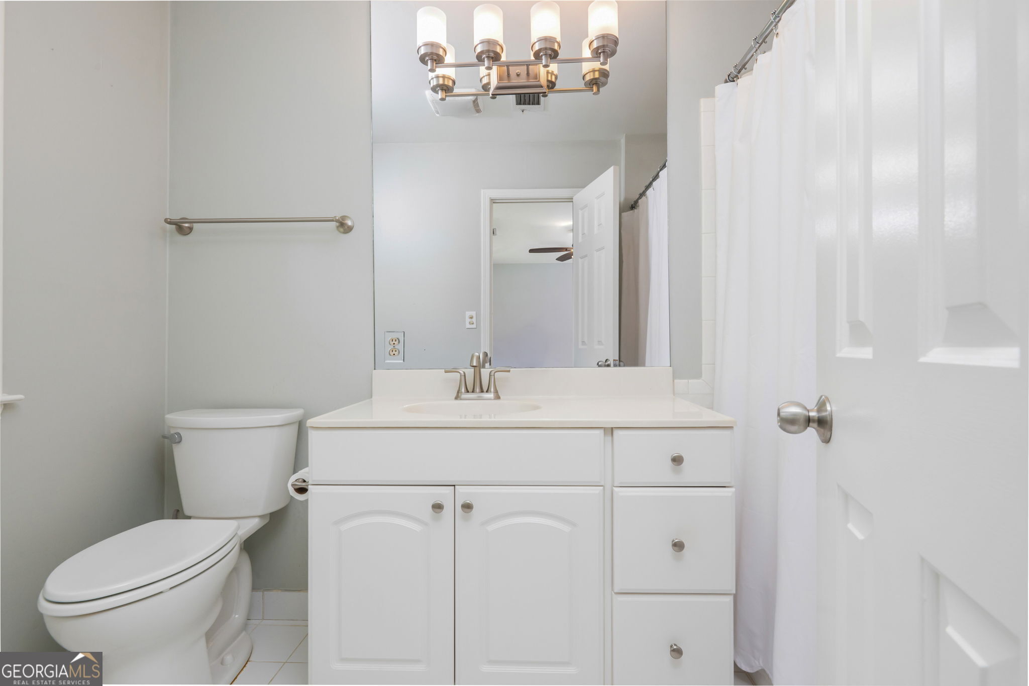 Bathroom with white vanity, large mirror, toilet, and curtained shower.