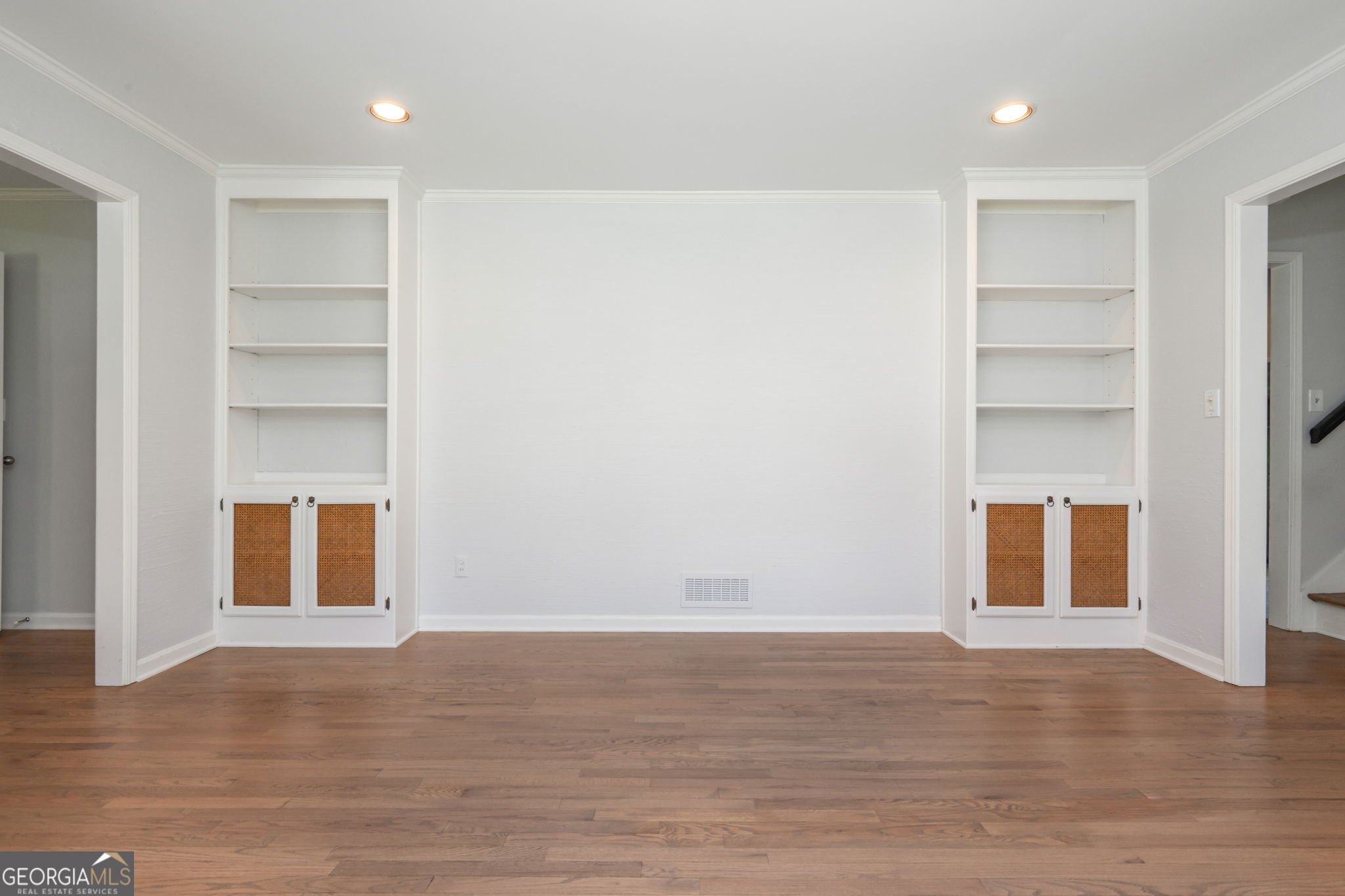 Empty room with hardwood floors and matching built-in shelves with cane-front cabinets.