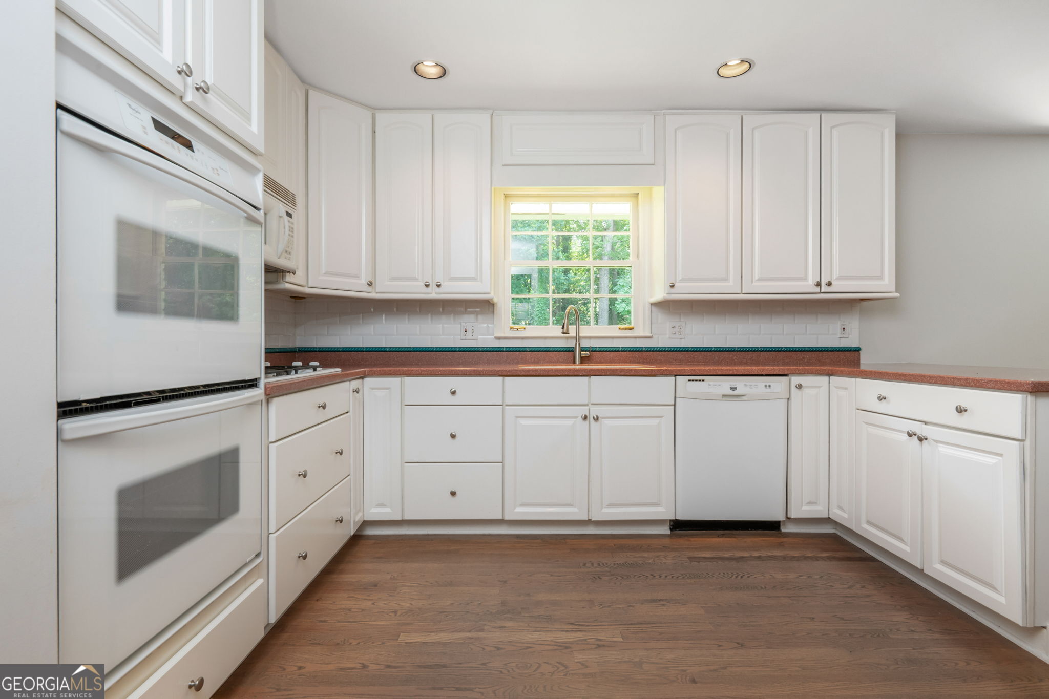Kitchen with white cabinetry, brown countertops, a window above the sink, and dark wood floors.
