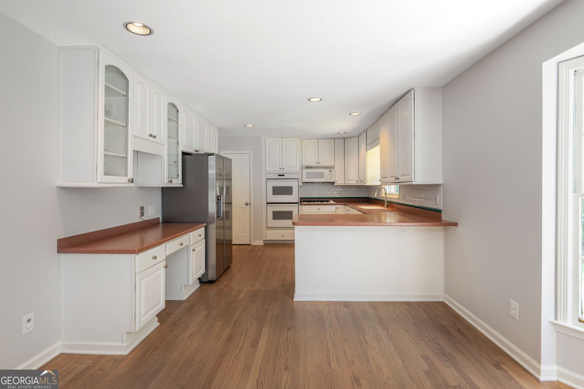Kitchen with white cabinetry, a reddish-brown peninsula, stainless steel refrigerator, and wood flooring.