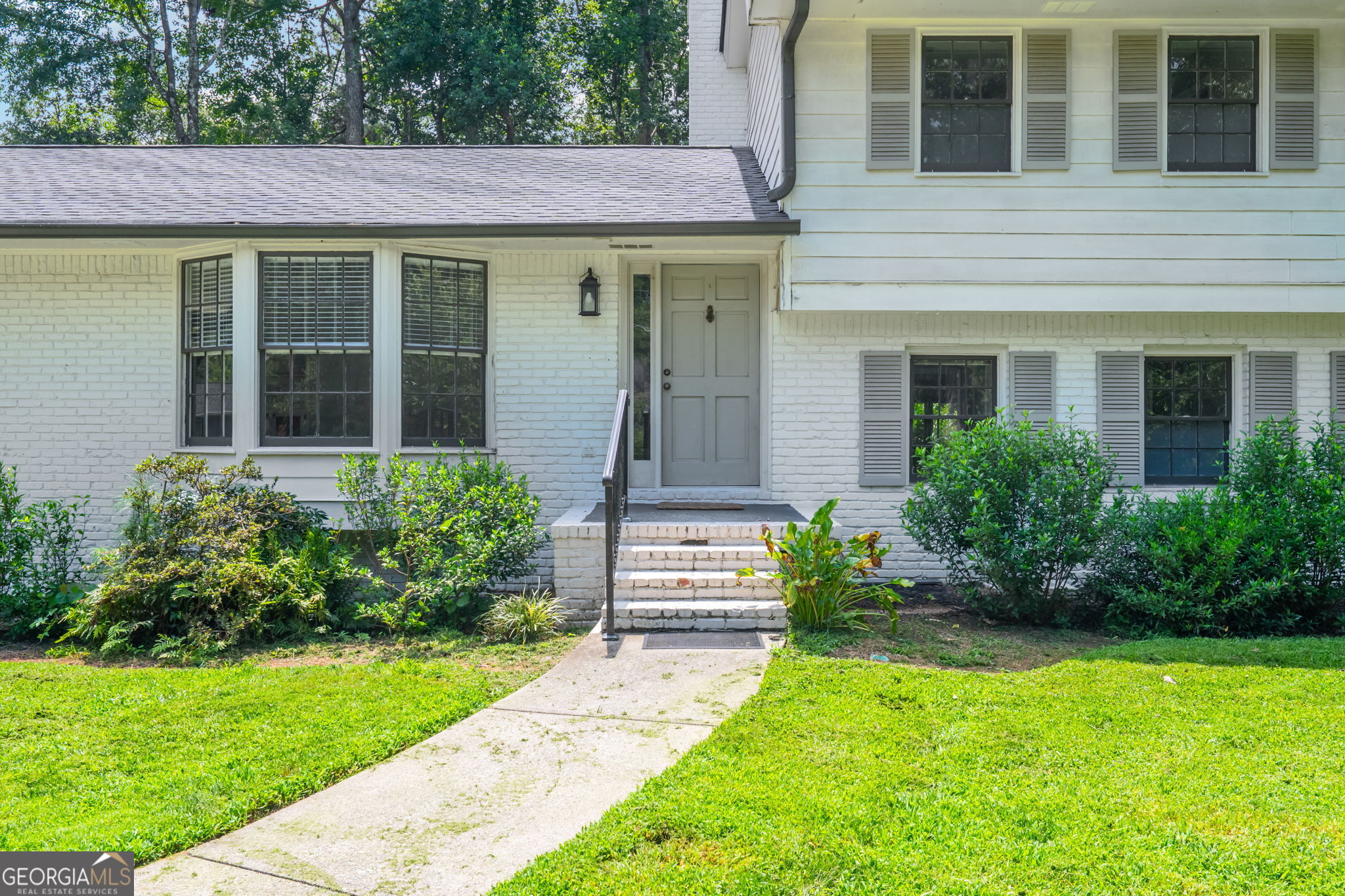 White brick home with gray shutters, bay window, front steps, and a walkway through the lawn.