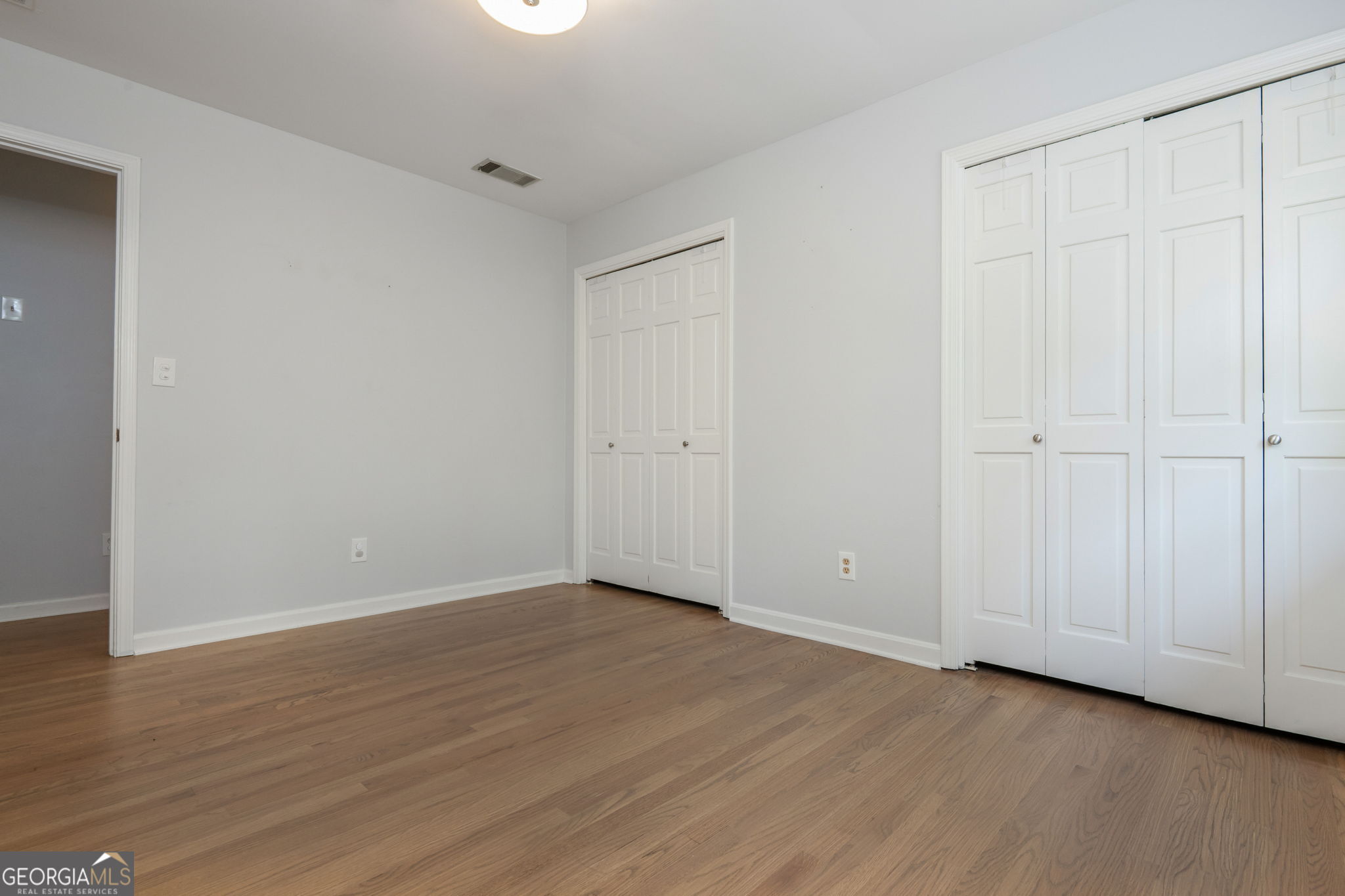 Vacant bedroom with hardwood floors and multiple white paneled closets.