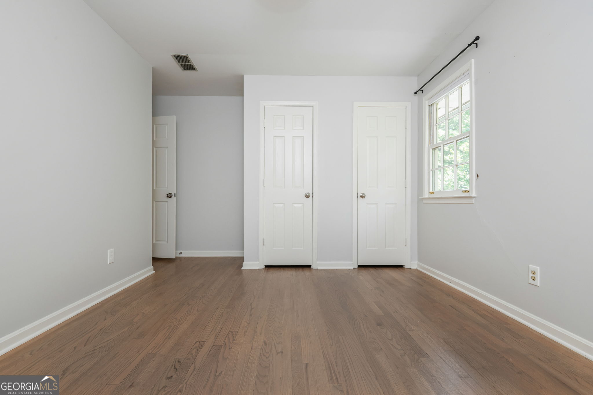 Empty room with hardwood floors, two closed doors, and a sunlit window.