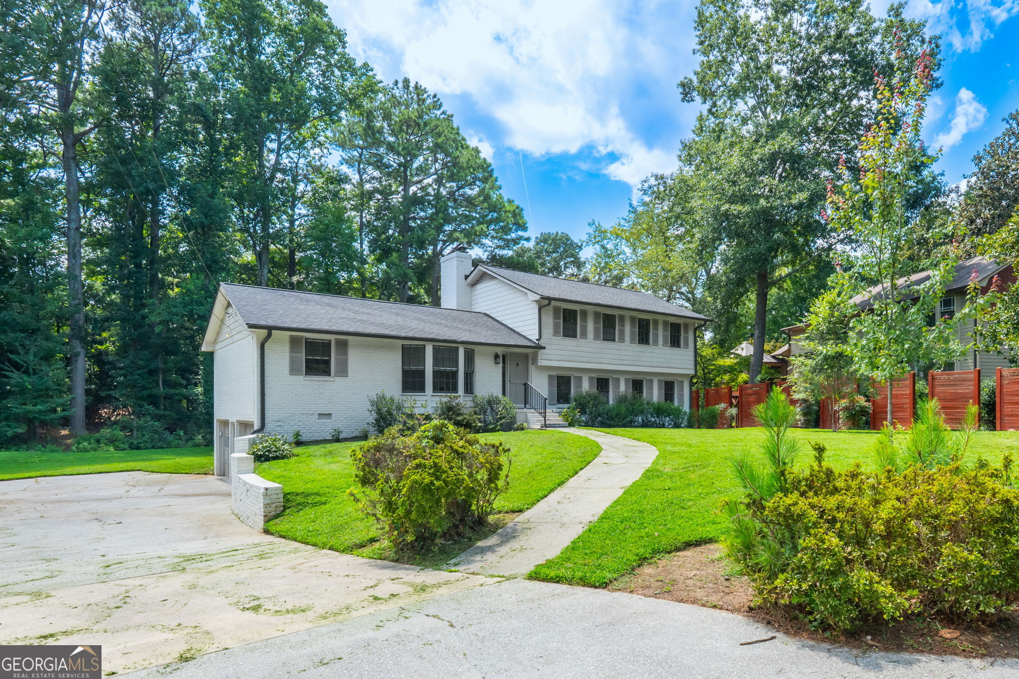White brick two-story home with a curved walkway, broad driveway, and mature trees.